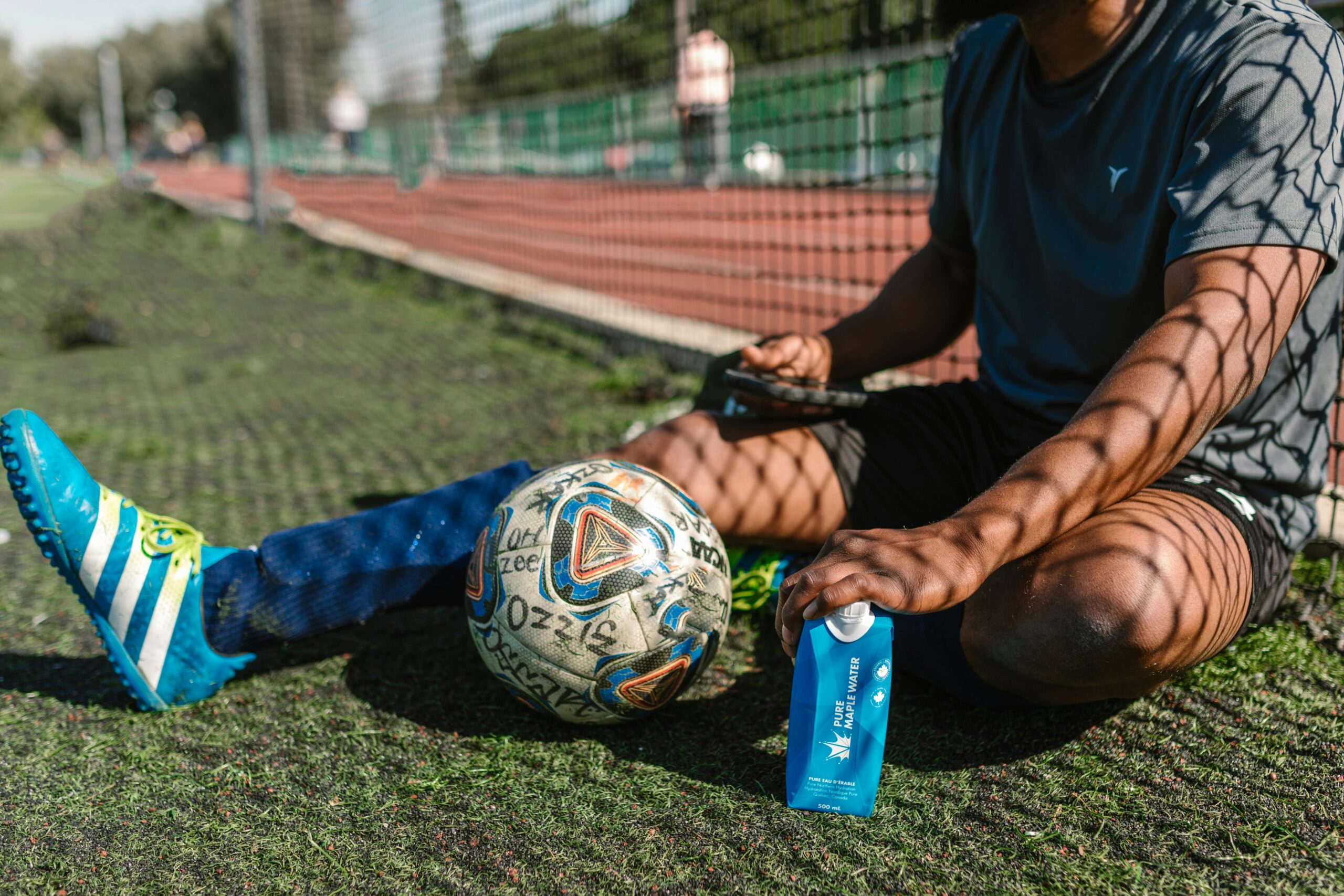 A soccer player takes a break, sitting on a grassy field with a soccer ball and water bottle.
