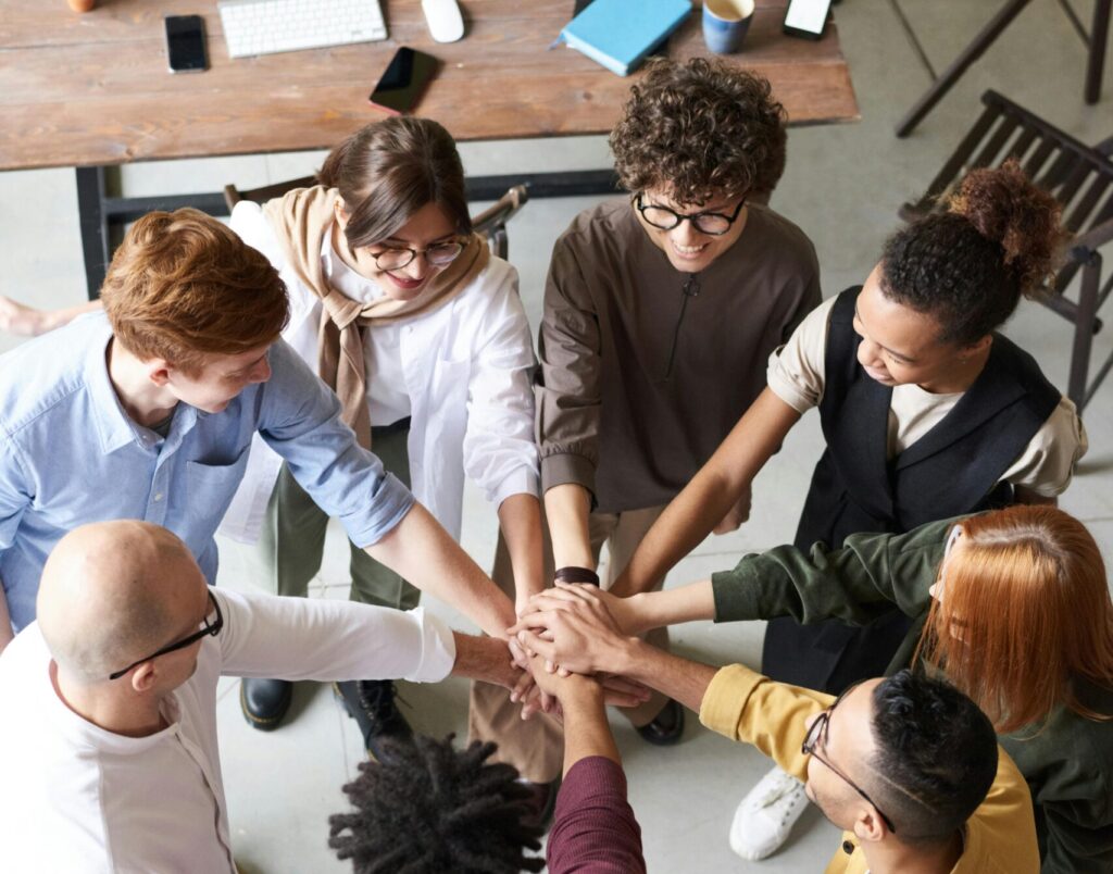 A diverse group of professionals joins hands in a team-building exercise indoors.